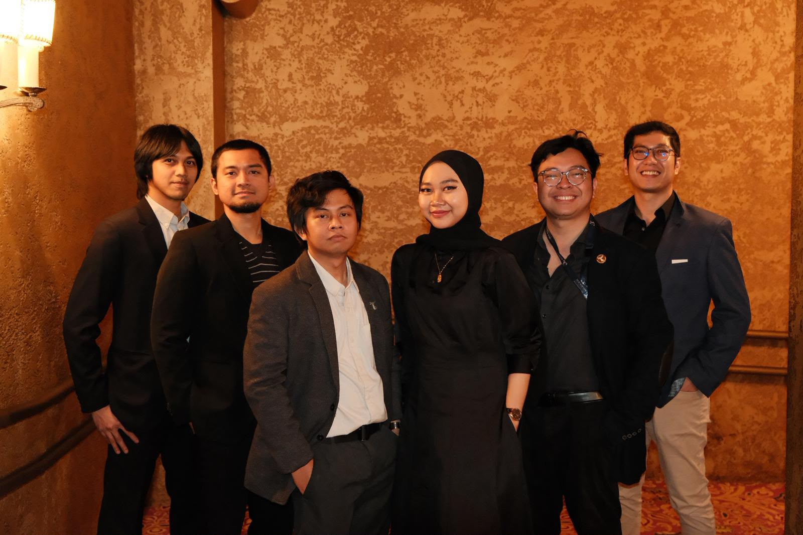 Six members of the Jaya team together against a gold wall